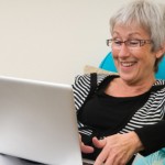Senior woman working on a laptop, sitting relaxed on the couch.